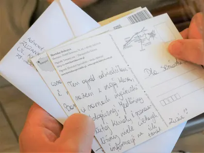 Dłonie trzymają pocztówkę z odręcznym tekstem zaadresowaną Dla Seniorki