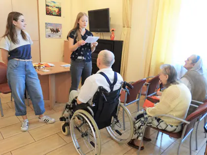 Dwie dziewczyny czytają listy mieszkańcom siedzącym w świetlicy