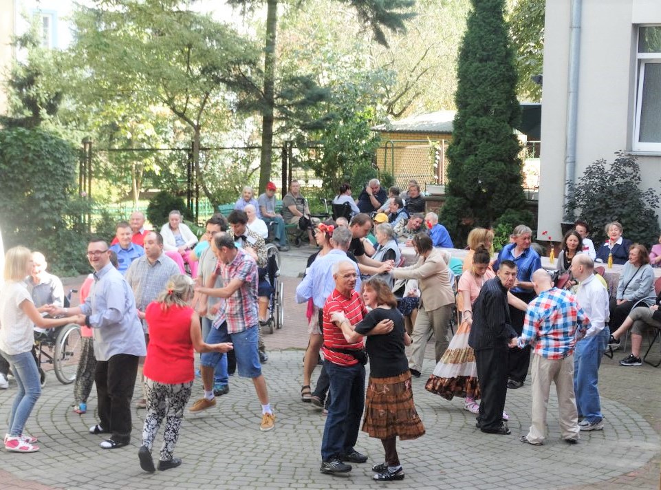 Mieszkańcy i goście tańczą na dziedzińcu Domu podczas pikniku.