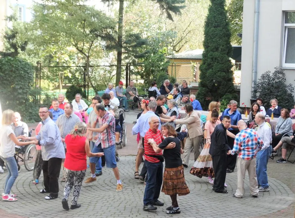 Mieszkańcy i goście tańczą na dziedzińcu Domu podczas pikniku.