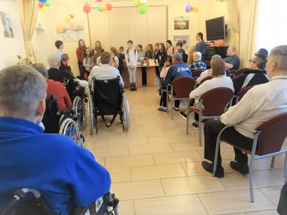 Dzieci występują w głębi świetlicy, mieszkańcy siedzą na wózkach i krzesłach