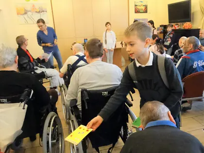 Chłopiec wręcza kartkę mieszkańcowi na wózku