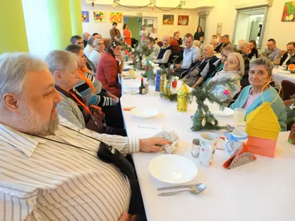 Starszy mieszkaniec przy wigilijnym stole, w głębi pozostali uczestnicy