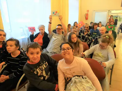 Uczniowie i mieszkańcy śpiewają kolędy, niektórzy unoszą kolorowe kartki