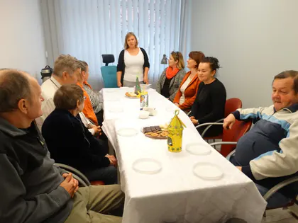 Mieszkańcy i pracownice siedzą przy długim stole nakrytym białym obrusem