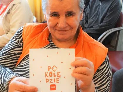Uśmiechnięta mieszkanka w pomarańczowej kamizelce trzyma broszurę Po kolędzie