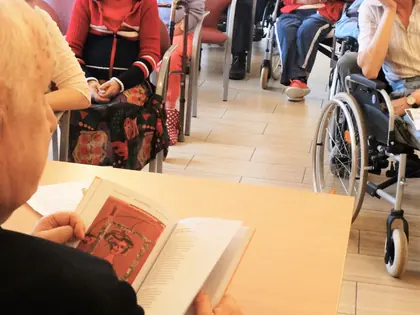 Mężczyzna czyta książkę, w tle mieszkańcy słuchają