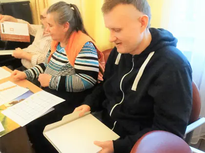 Mieszkanka i mieszkaniec w bluzie grają przy stole, czytając karty