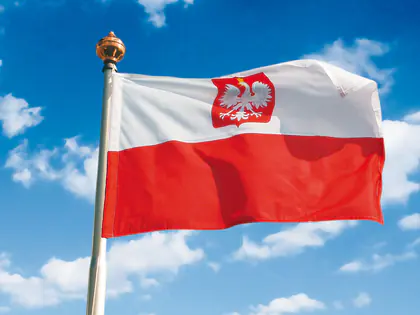 Biało-czerwona flaga z godłem na maszcie na tle nieba