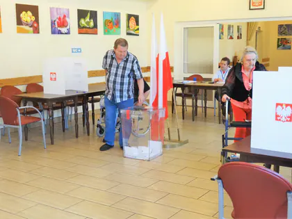 Mieszkańcy głosują w lokalu wyborczym przy biało-czerwonych flagach