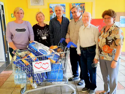 Mieszkańcy i opiekunki stoją przy wózku sklepowym pełnym zakupów od darczyńcy