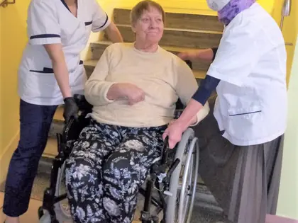 Opiekunki pomagają mieszkance na wózku przy schodach