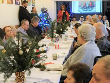 Kobieta przemawia przy choince do mieszkańców przy wigilijnym stole