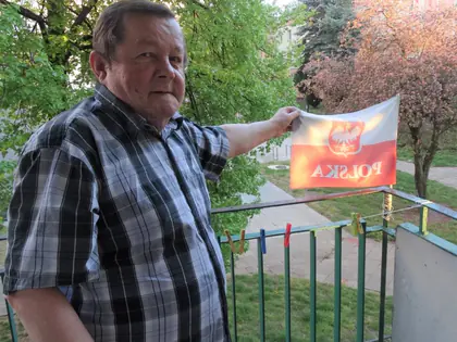 Mężczyzna na balkonie trzyma flagę Polski z godłem