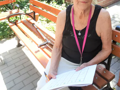 Mieszkanka siedzi na ławce w ogrodzie z kartą do gry w bingo na kolanach