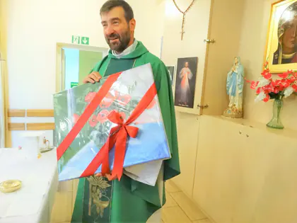 Kapelan w zielonym ornacie w kaplicy trzyma prezent przewiązany czerwoną wstążką