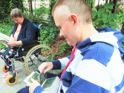 Mieszkaniec ogląda fotografie, obok mieszkanka na wózku