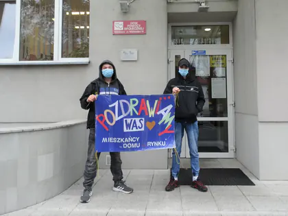 Młodzież trzyma przed Domem transparent z napisem Pozdrawiamy Was, Mieszkańcy Domu przy Rynku