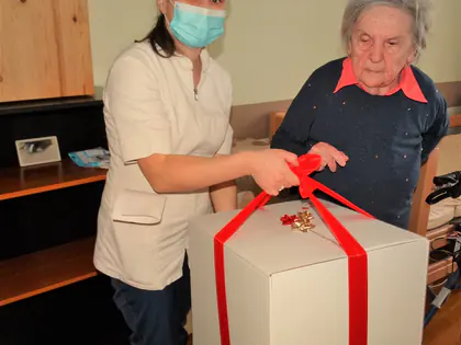 Opiekunka w czapce Mikołaja i mieszkanka z dużym prezentem z czerwoną kokardą