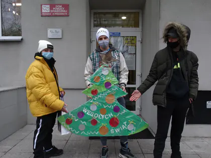 Młodzież trzyma przed Domem dużą papierową choinkę z napisem Wesołych Świąt