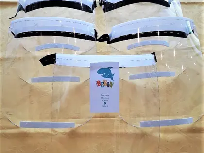 Przezroczyste przyłbice ochronne ułożone na stole, na jednej wizytówka fundacji Rekin