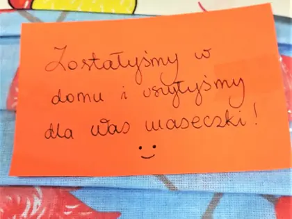 Liścik na stosie maseczek z napisem Zostaliśmy w domu i uszyliśmy dla was maseczki