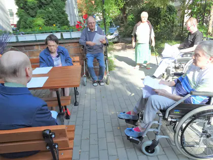 Mieszkańcy czytają przy drewnianych stołach w ogrodzie