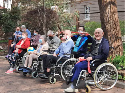 Mieszkańcy na wózkach ćwiczą z taśmami i piłką w ogrodzie