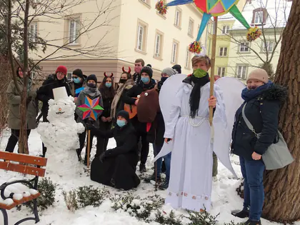 Kolędnicy pozują przy bałwanie na zaśnieżonym podwórku