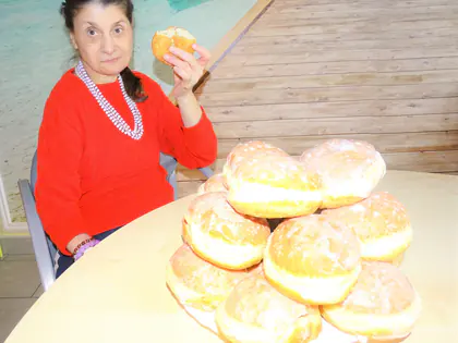 Mieszkanka w czerwonym swetrze trzyma pączka nad talerzem pączków