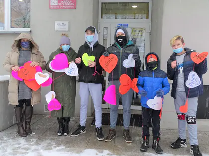 Młodzież z Domu przy Rynku trzyma łańcuch z kolorowych papierowych serc przed wejściem do Domu