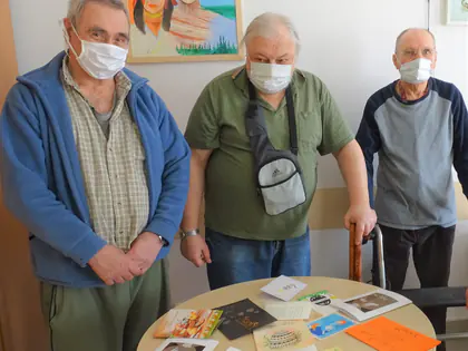 Trzej mieszkańcy w maseczkach stoją przy stoliku z kartkami świątecznymi