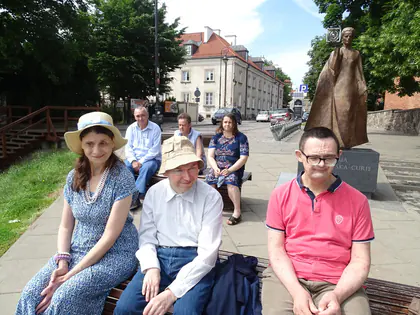 Mieszkańcy odpoczywają na ławce przy pomniku Marii Skłodowskiej-Curie