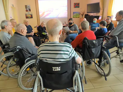 Mieszkańcy na wózkach siedzą w kręgu podczas zajęć relaksacyjnych