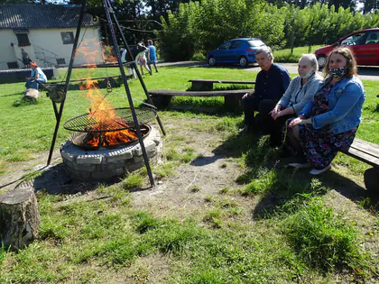 Mieszkańcy siedzą na ławkach przy ognisku na trawie
