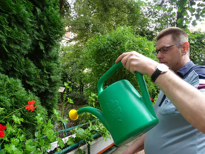 Mieszkaniec podlewa kwiaty zieloną konewką w ogrodzie sensorycznym