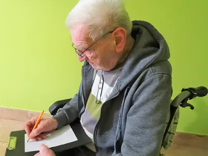 Mieszkaniec na wózku pisze list na podkładce
