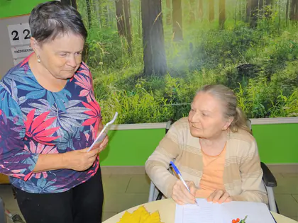 Mieszkanka pomaga drugiej pisać przy stole z jesiennymi liśćmi