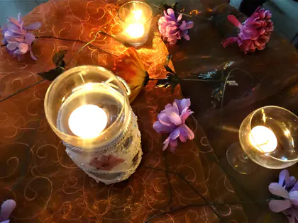 Zapalone świece w szklanych lampionach i fioletowe kwiaty na stole