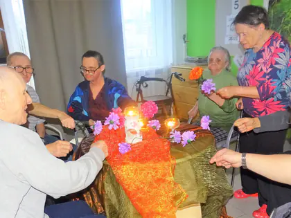 Mieszkańcy przy stole ze zniczami i kwiatami podczas wspomnień o zmarłych