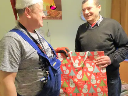 Mężczyzna w czapce Mikołaja wręcza mieszkańcowi świąteczną torbę