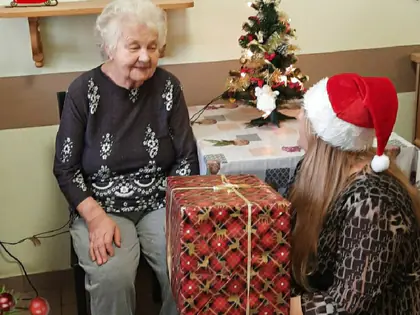 Kobieta w czapce Mikołaja wręcza mieszkance prezent w świątecznym papierze
