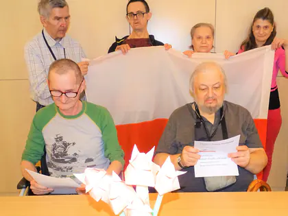 Mieszkańcy trzymają biało-czerwoną flagę przy stole