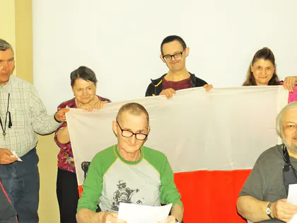 Mieszkańcy trzymają biało-czerwoną flagę i kartki z tekstem pieśni