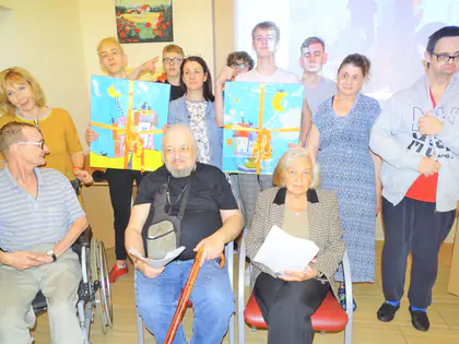 Młodzież z Domu przy Rynku i mieszkańcy pozują z kolorowymi obrazami