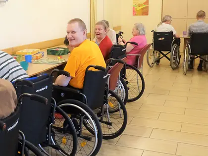 Mieszkańcy na wózkach przy stołach z grami w świetlicy