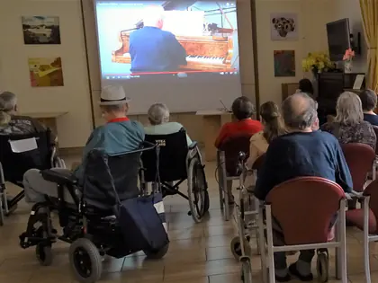 Mieszkańcy na wózkach oglądają na ekranie nagranie pianisty grającego na fortepianie
