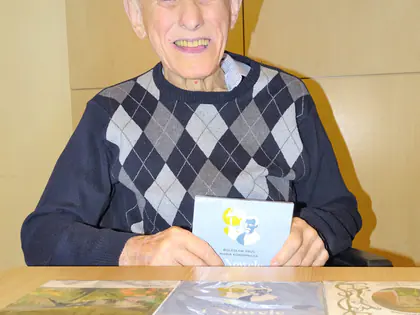 Uśmiechnięty mieszkaniec trzyma audiobook, przed nim na stole leżą płyty z audiobookami