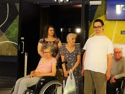 Mieszkańcy, jedna na wózku, i opiekunka stoją w holu kina