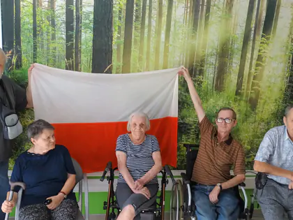Mieszkańcy trzymają biało-czerwoną flagę na tle fototapety z lasem